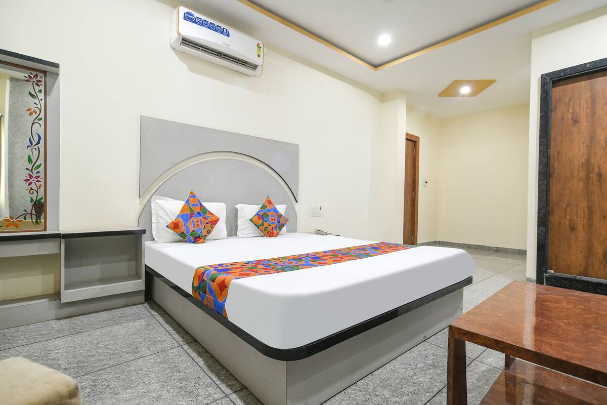 Een hotelkamer met een bed, nachtkastje, spiegel en airconditioning.