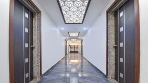 A hallway with dark wooden doors, a marble floor, and a decorative ceiling light fixture. - Fabhotel Maan Palace (Ahmedabad)