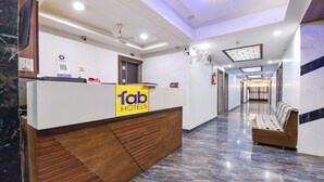 A hotel reception area with a wooden reception desk, a sign for 'Tab Hotels', and a marble floor. - Fabhotel Maan Palace (Ahmedabad)