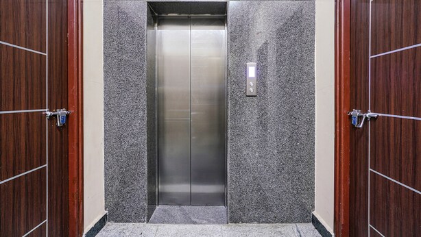 An elevator with a metallic interior, flanked by wooden doors with visible numbers. - Fabexpress D Grand (Hyderabad)