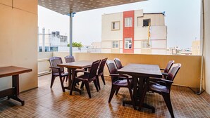 A dining area with tables and chairs, a tiled floor, and a view of buildings in the background. - Fabexpress D Grand (Hyderabad)