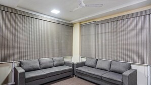 A waiting area with two grey sofas, a ceiling fan, and blinds on the windows. - Fabexpress D Grand (Hyderabad)