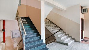A staircase with blue steps and a wooden handrail, leading to a landing with a white wall and a red pipe. - FabHotel Surya Palace 2 (Chandigarh)