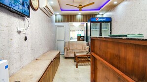 A lobby with a reception desk, a sofa, a television mounted on the wall, and a ceiling fan. - FabHotel Surya Palace 2 (Chandigarh)