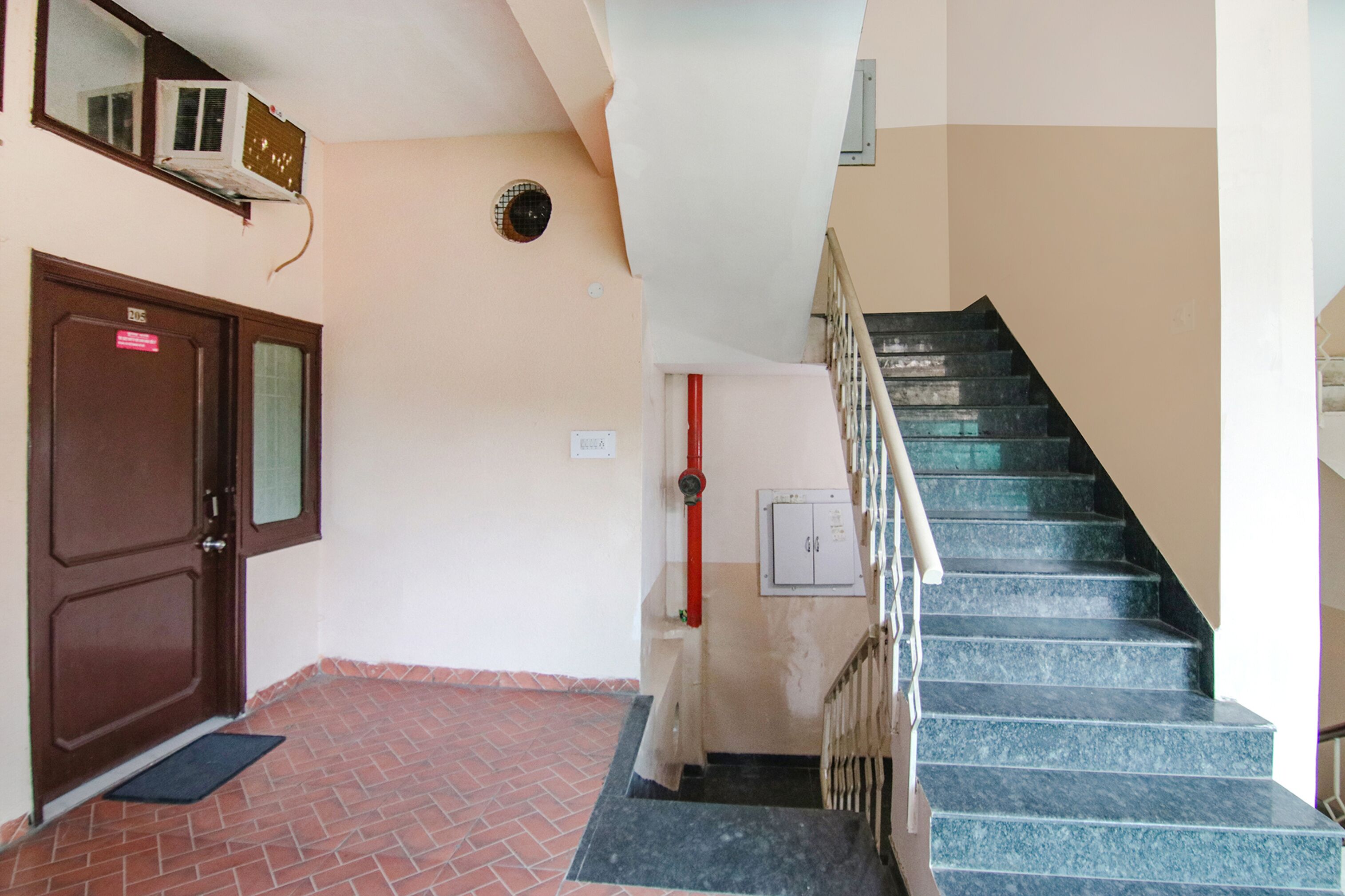 Un escalier avec une rampe en métal, une porte marron avec une fenêtre et un tuyau rouge sur le mur.