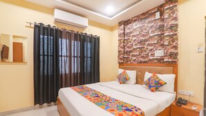 Habitación de hotel con cama, mesita de noche, aire acondicionado, ventana con cortinas y una pared con diseño decorativo.