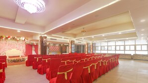 Un salón amplio con filas de sillas rojas, un escenario con adornos florales y ventanas grandes que dejan entrar luz natural.