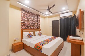 A hotel room with a bed, bedside table, nightstand, ceiling fan, air conditioning unit, and a curtain. - Fabhotel Swarn Banquet (Varanasi)