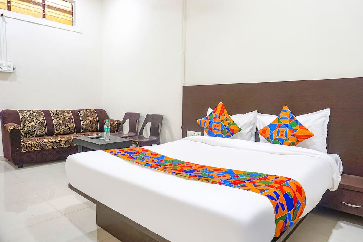 A hotel room with a large bed, a sofa, two armchairs, and a small table with a bottle.
