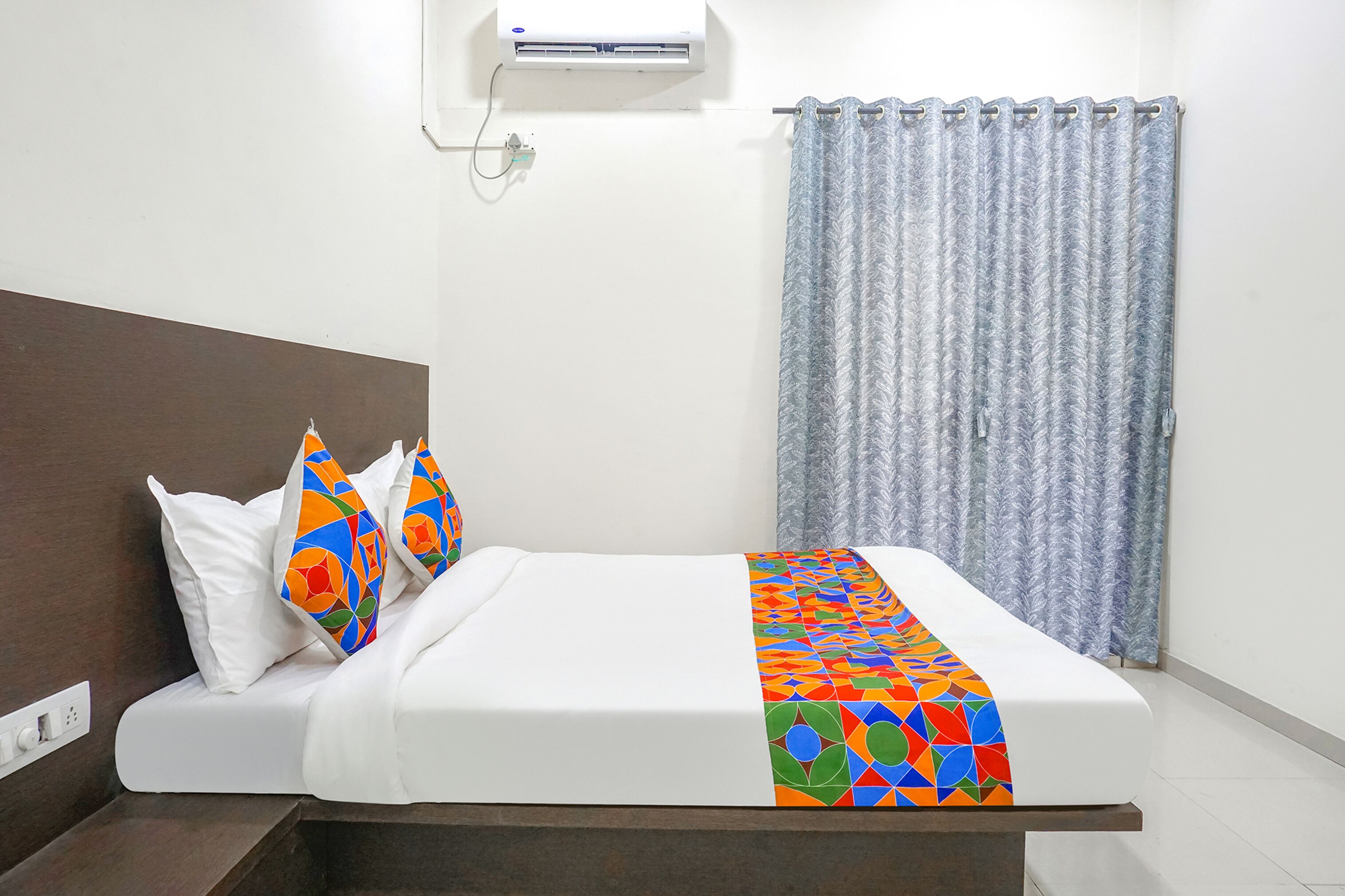 Un lit bien fait, avec un matelas blanc et une couvre-lit aux motifs géométriques colorés.