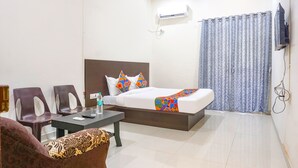 A hotel room with a bed, a desk, two chairs, a sofa, and an air conditioning unit. - FabHotel Om Sai I (Nashik)