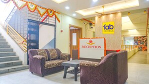 A hotel reception area with a staircase, reception desk, and sofas. - FabHotel Om Sai I (Nashik)