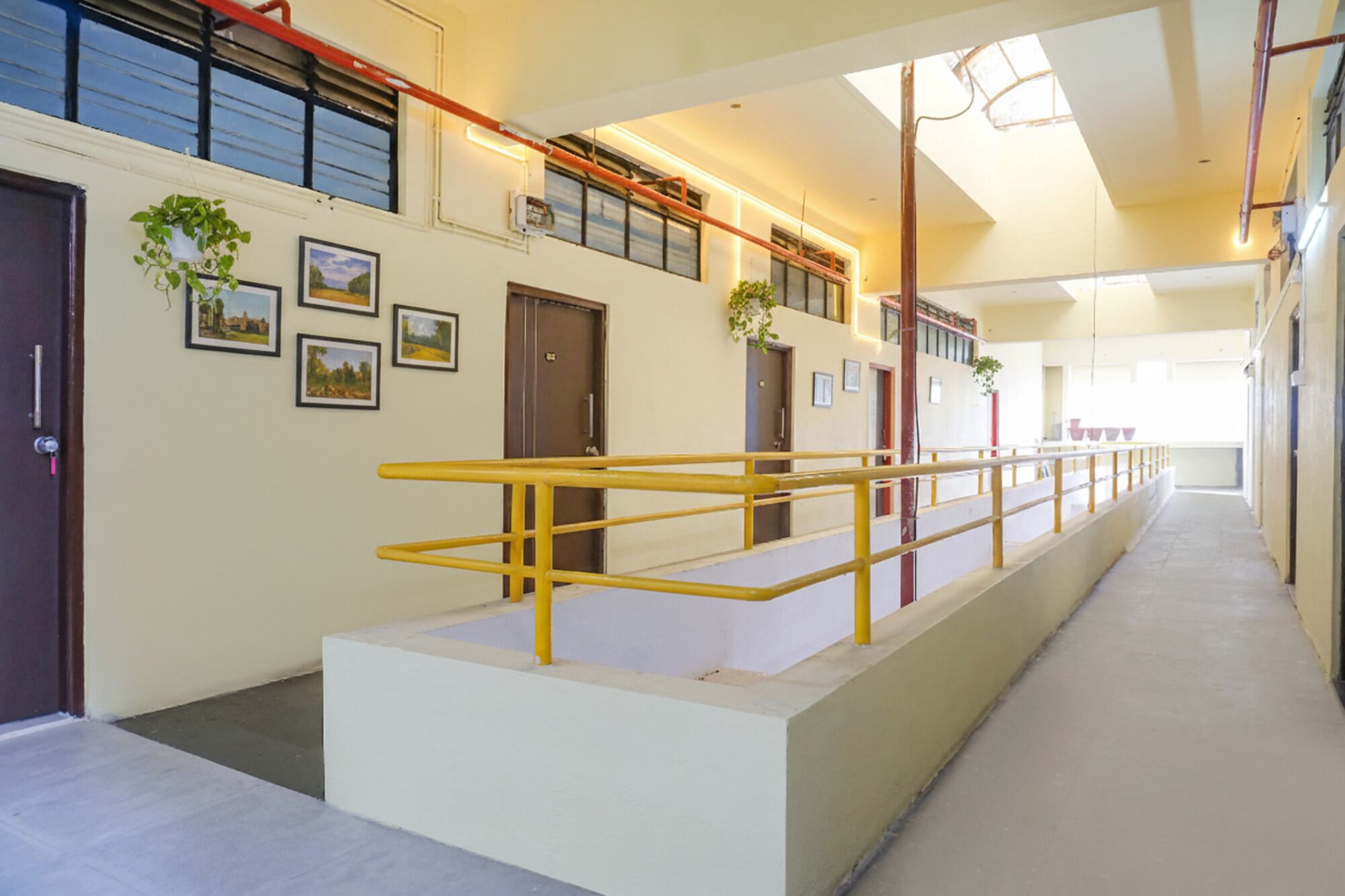 A corridor with a yellow railing, doors, and framed pictures on the walls.