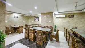 A dining area with marble walls, wooden furniture, and ceiling fans. - FabHotel Belwood (New Delhi)