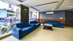 A hotel lobby with blue sofas, a reception desk, and a view of the street outside. - FabHotel Belwood (New Delhi)