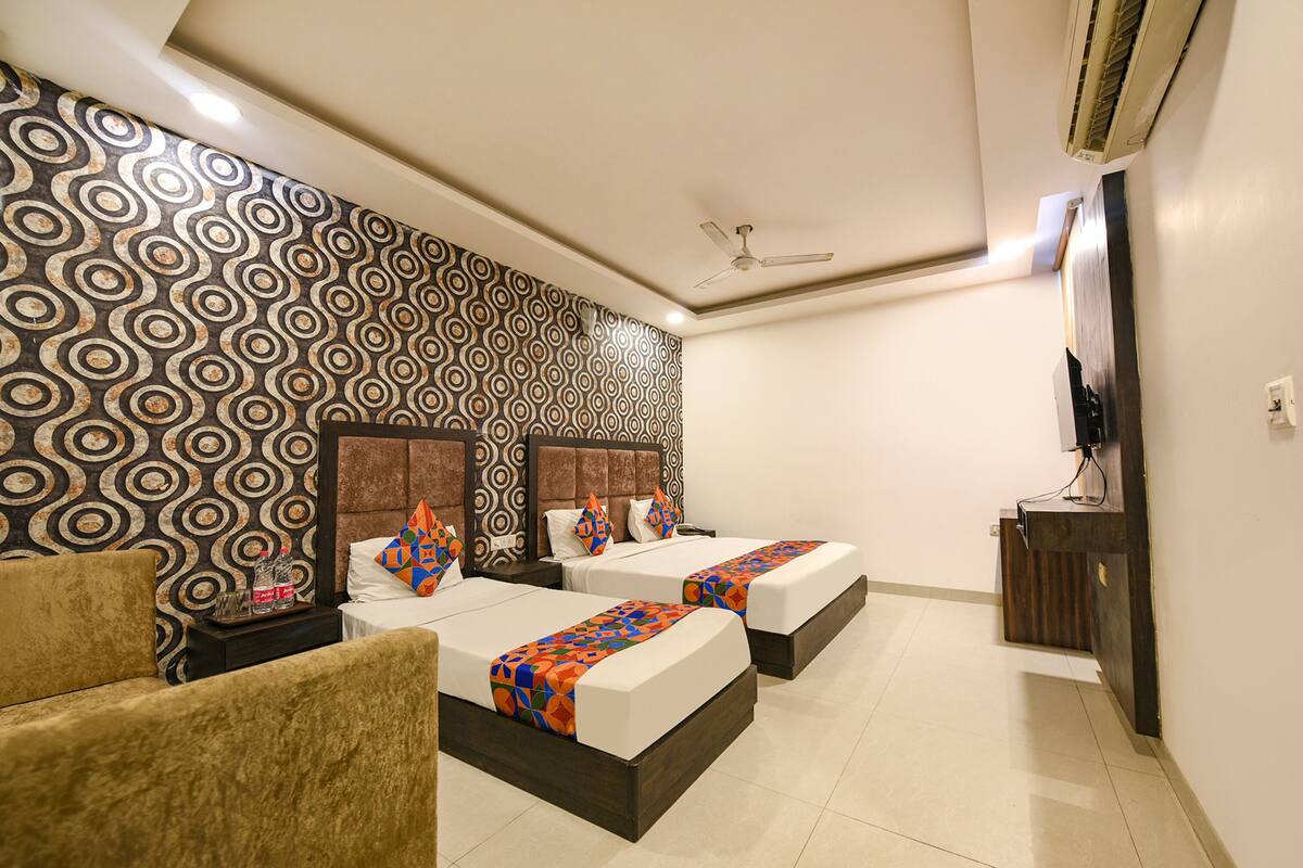 A hotel room with two beds, a sofa, a TV, and a patterned wall.