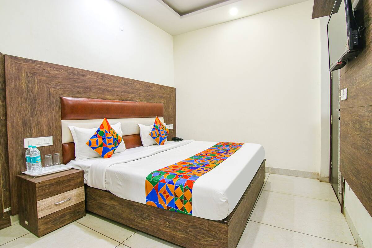 A neatly made bed with a colorful geometric-patterned bedspread, a wooden headboard, and a nightstand with a water bottle and glasses.