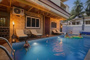 A swimming pool area with lounge chairs, a water feature, and a brick wall. - FabHotel Benz Destination (Candolim)