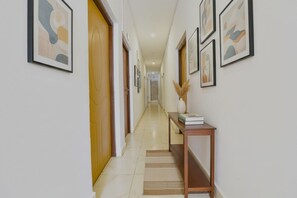 A hallway with framed abstract art on the walls, a wooden door, and a console table with a vase and books. - FabHotel Benz Destination (Candolim)