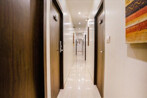 A hotel corridor with doors on both sides, a tiled floor, and a painting on the right wall. - Fabexpress Abad Inn (Mumbai)
