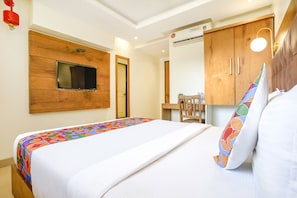 A hotel room with a bed, a TV mounted on the wall, a wooden wardrobe, and a desk with a chair. - Fabhotel Anam International (Mumbai)
