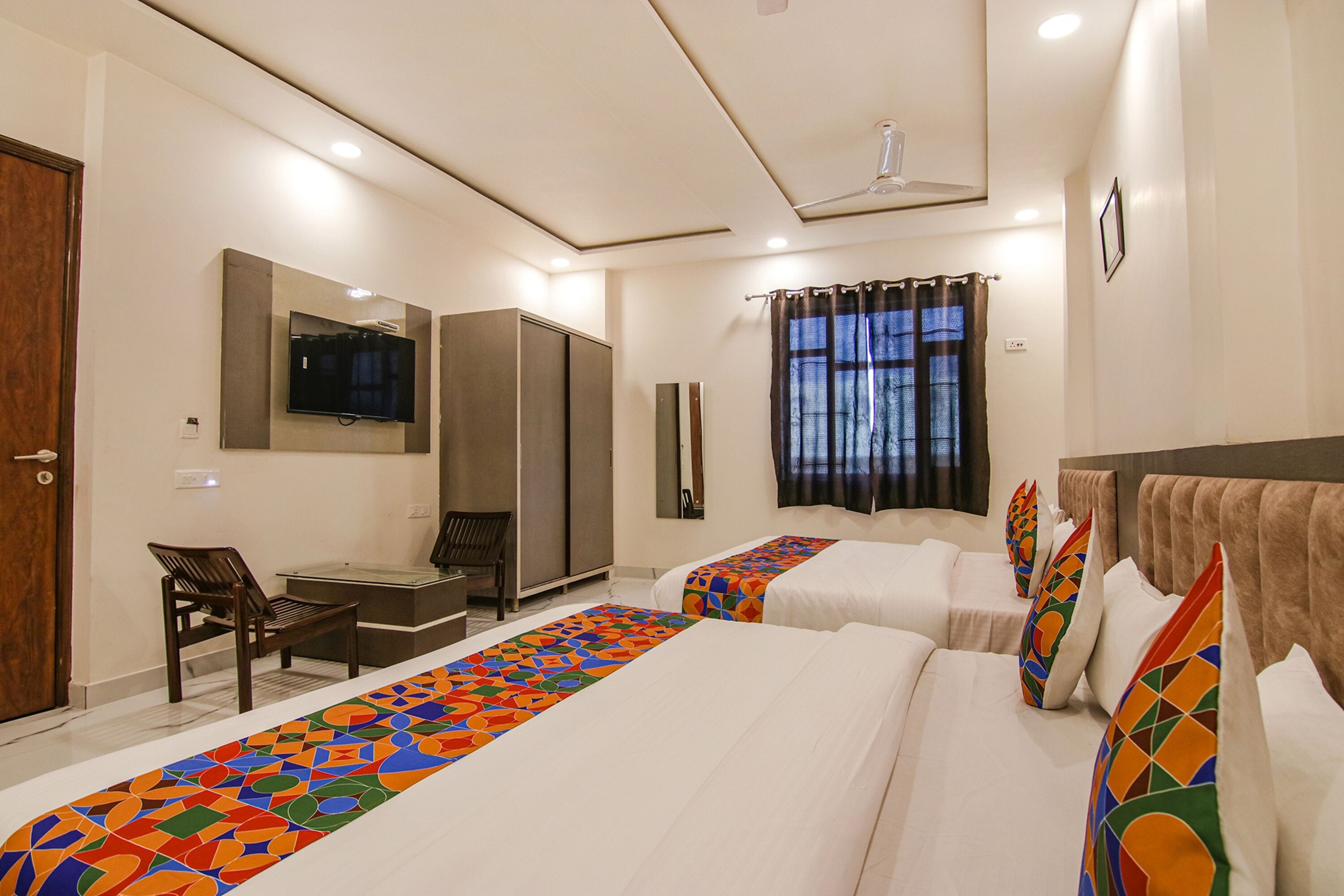 A hotel room with two beds, a desk, a chair, a television, and a wardrobe.