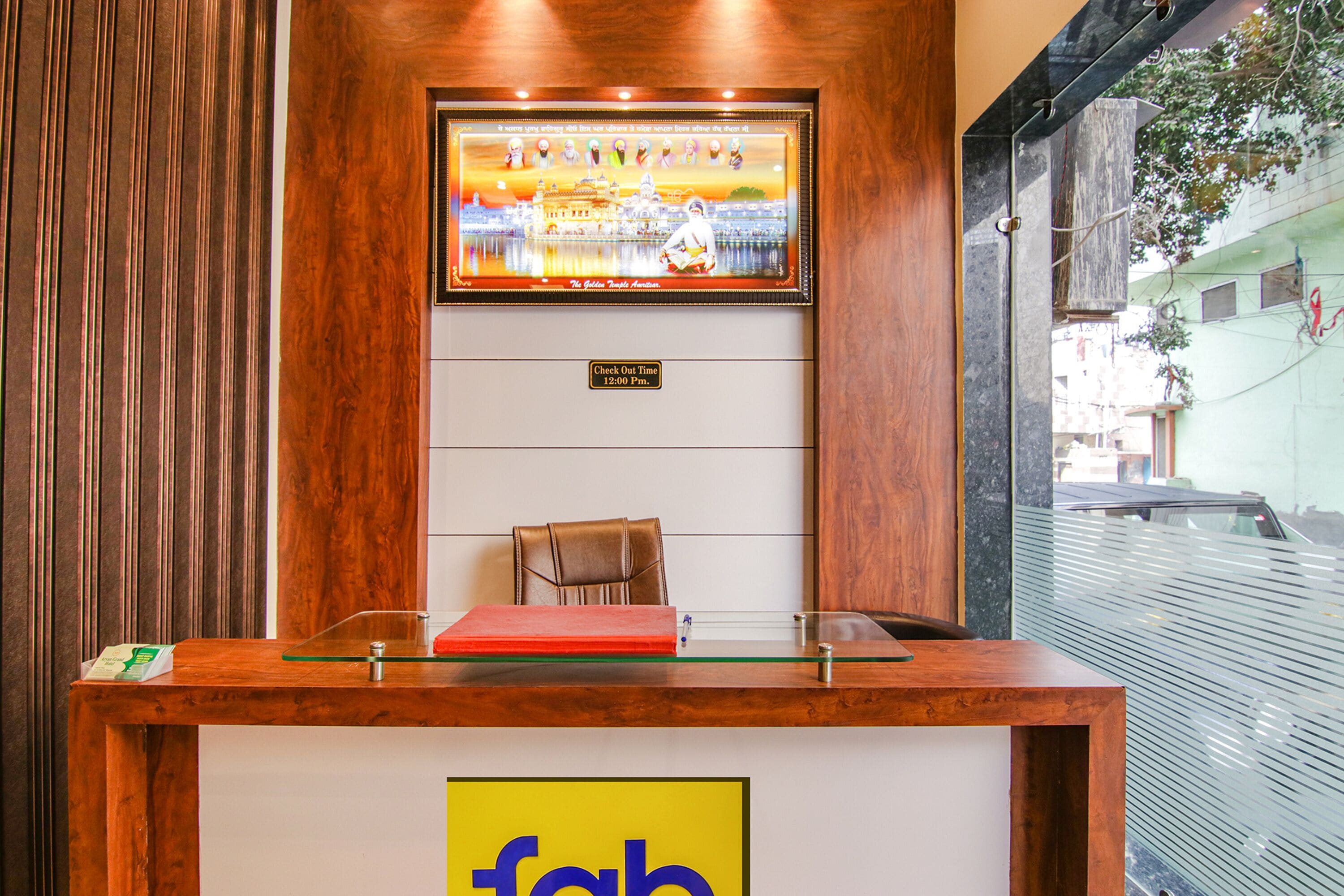 A reception desk with a framed picture above it, a check-out time sign, and a glass partition.