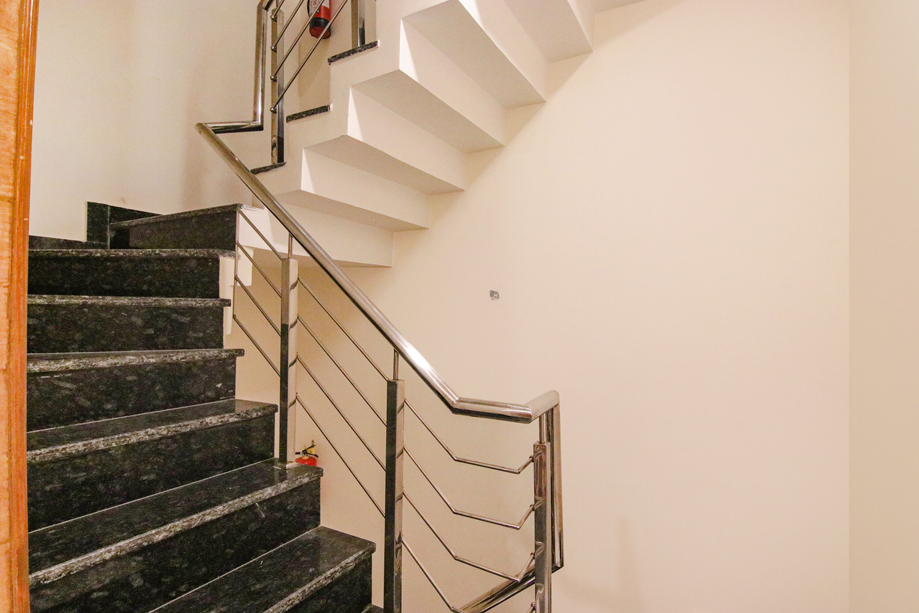 A modern staircase with black marble steps and a metal handrail, leading to a white landing area.