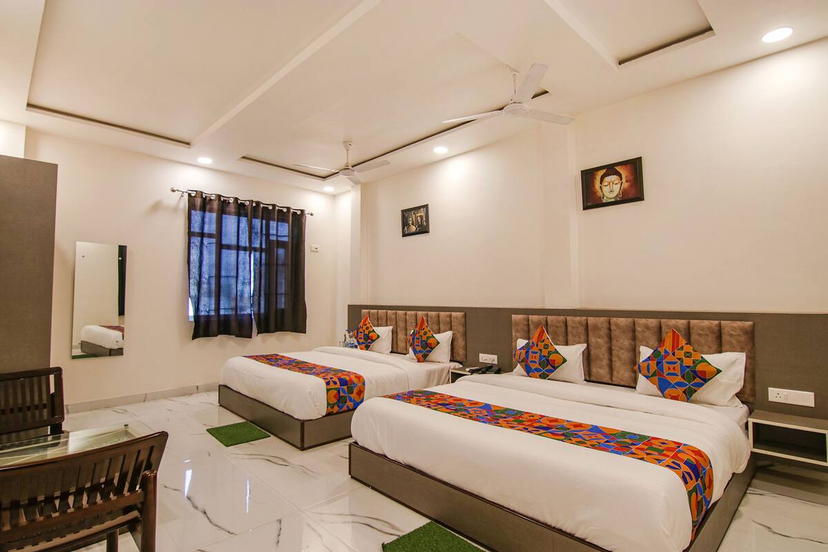 A hotel room with two beds, a ceiling fan, a window with curtains, a small table, and a chair.