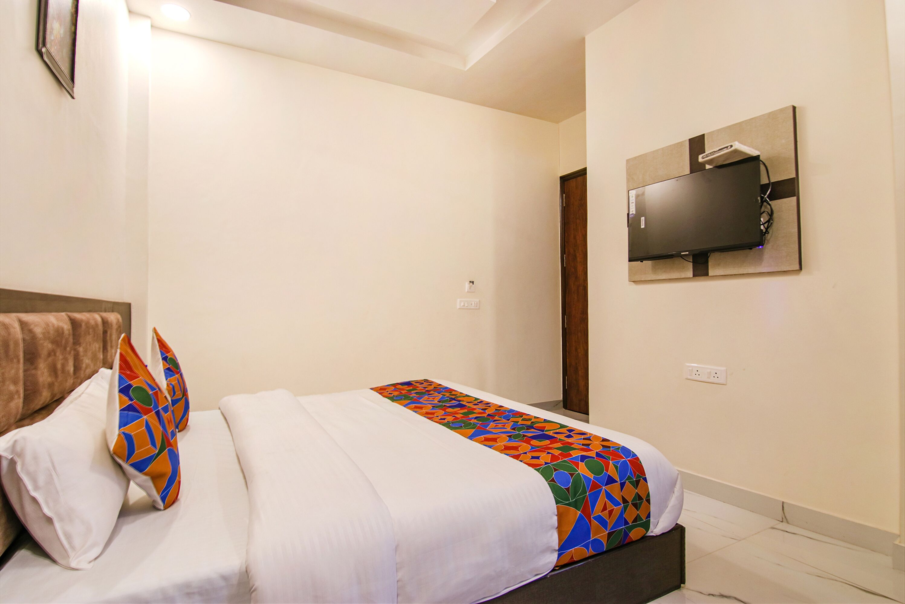 A hotel room with a bed, a TV mounted on the wall, and a door.