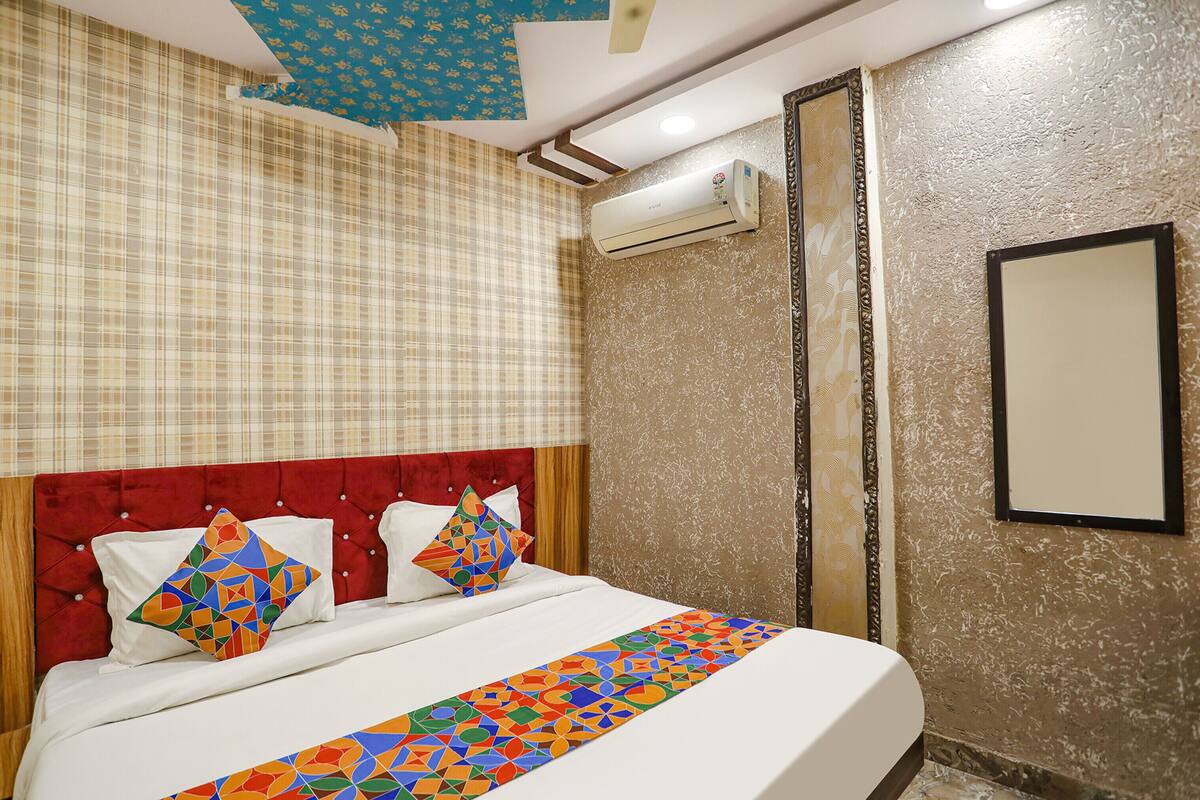 A hotel room with a red tufted headboard, a bed with white linens, colorful geometric pillows, and a patterned bed runner.