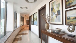 A modern hotel corridor with a marble floor, framed artwork on the walls, and a wooden console table with books and a vase. - Fabhotel Emerald (Ranchi)