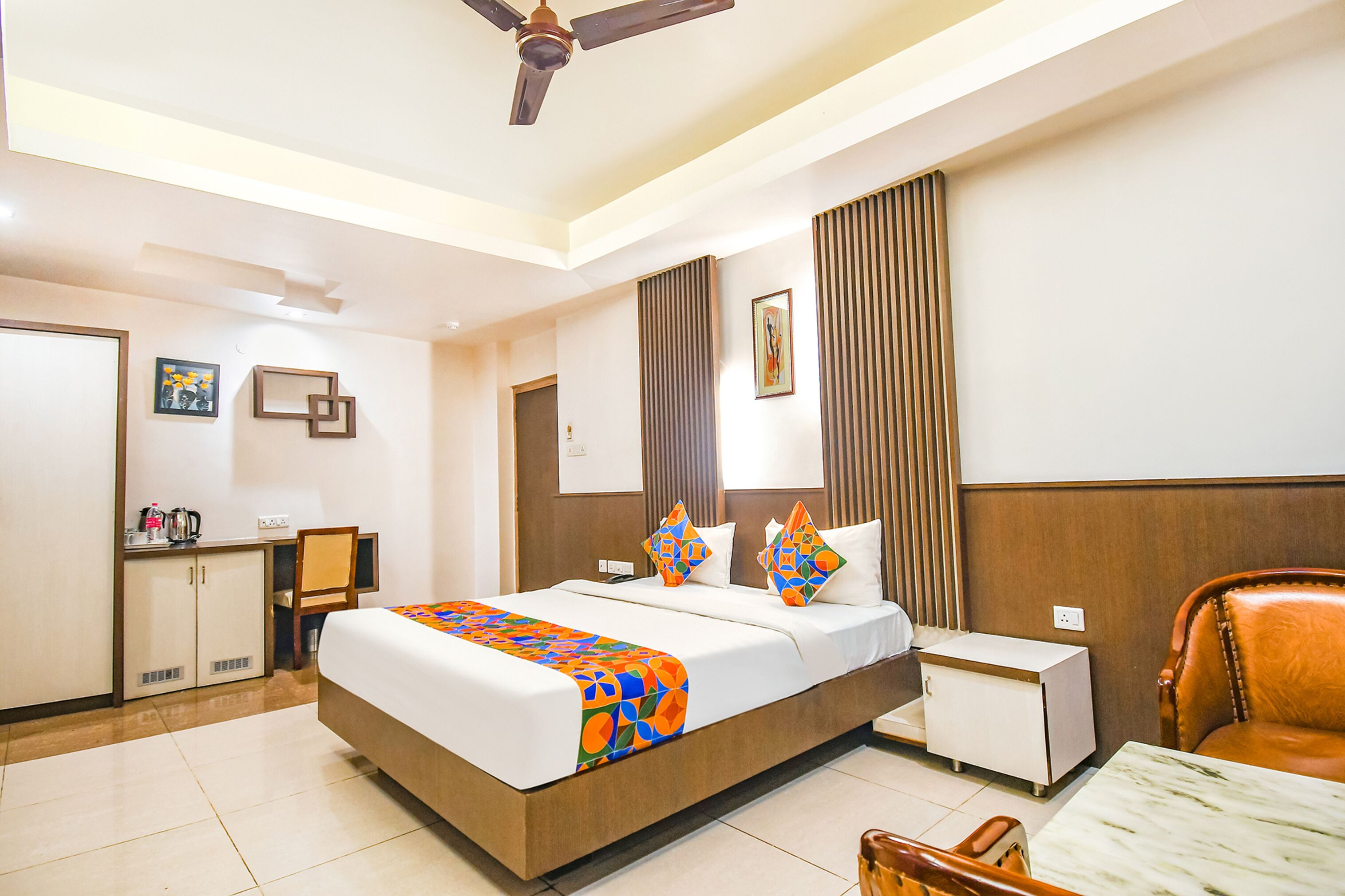 A hotel room with a bed, bedside table, chair, desk, wardrobe, and a ceiling fan.