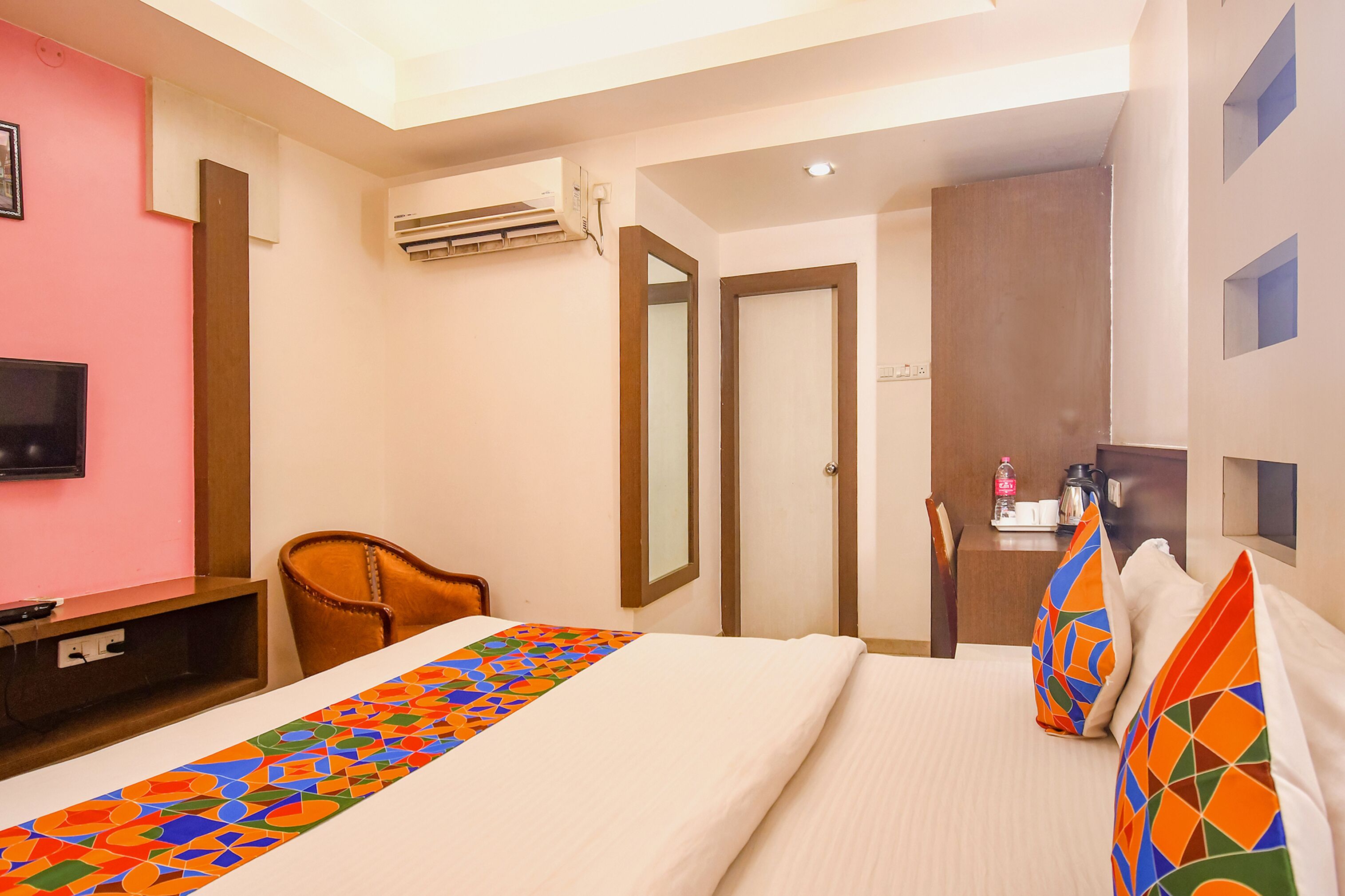 A hotel room with a bed, a desk, a chair, an air conditioning unit, and a television.