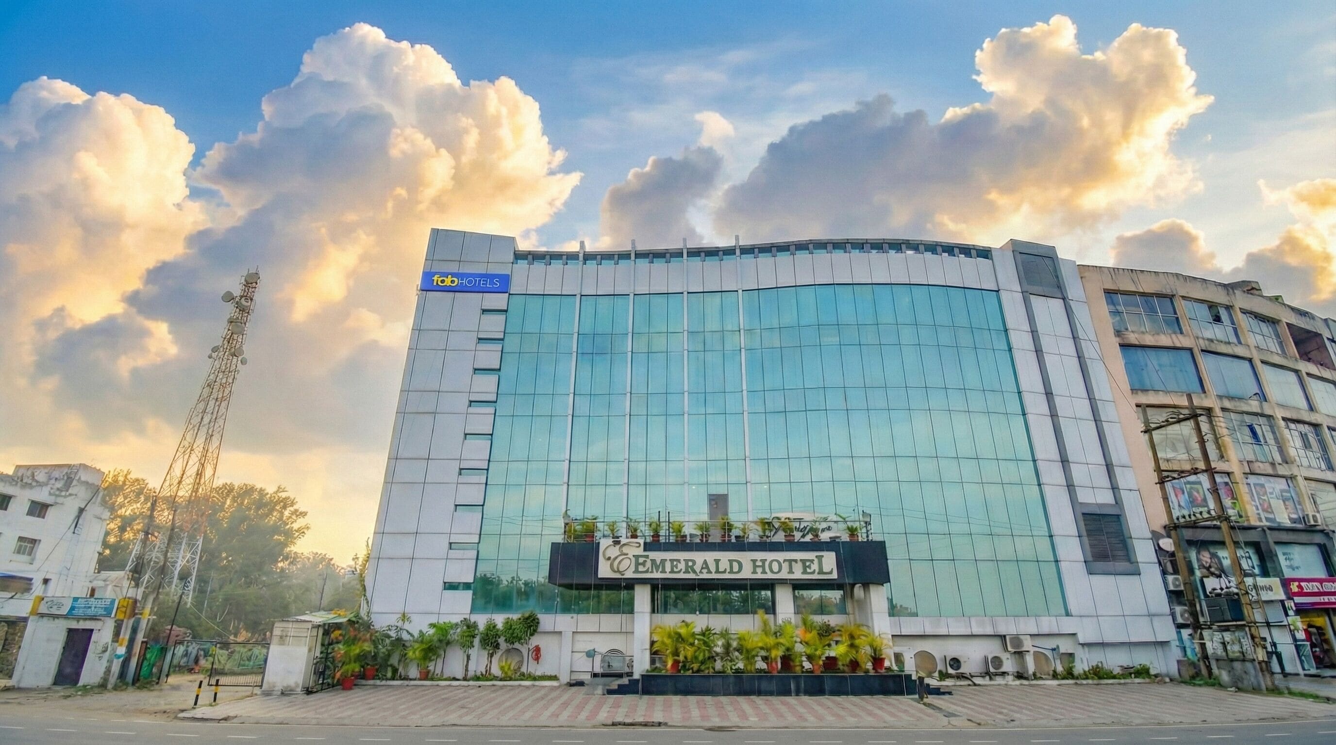 A hotel with a modern glass facade, a prominent sign for 'Emerald Hotel', and a landscaped entrance area.