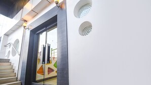 A modern building entrance with a glass door, a staircase, and a wall with circular cutouts. - Fabhotel Emerald (Ranchi)