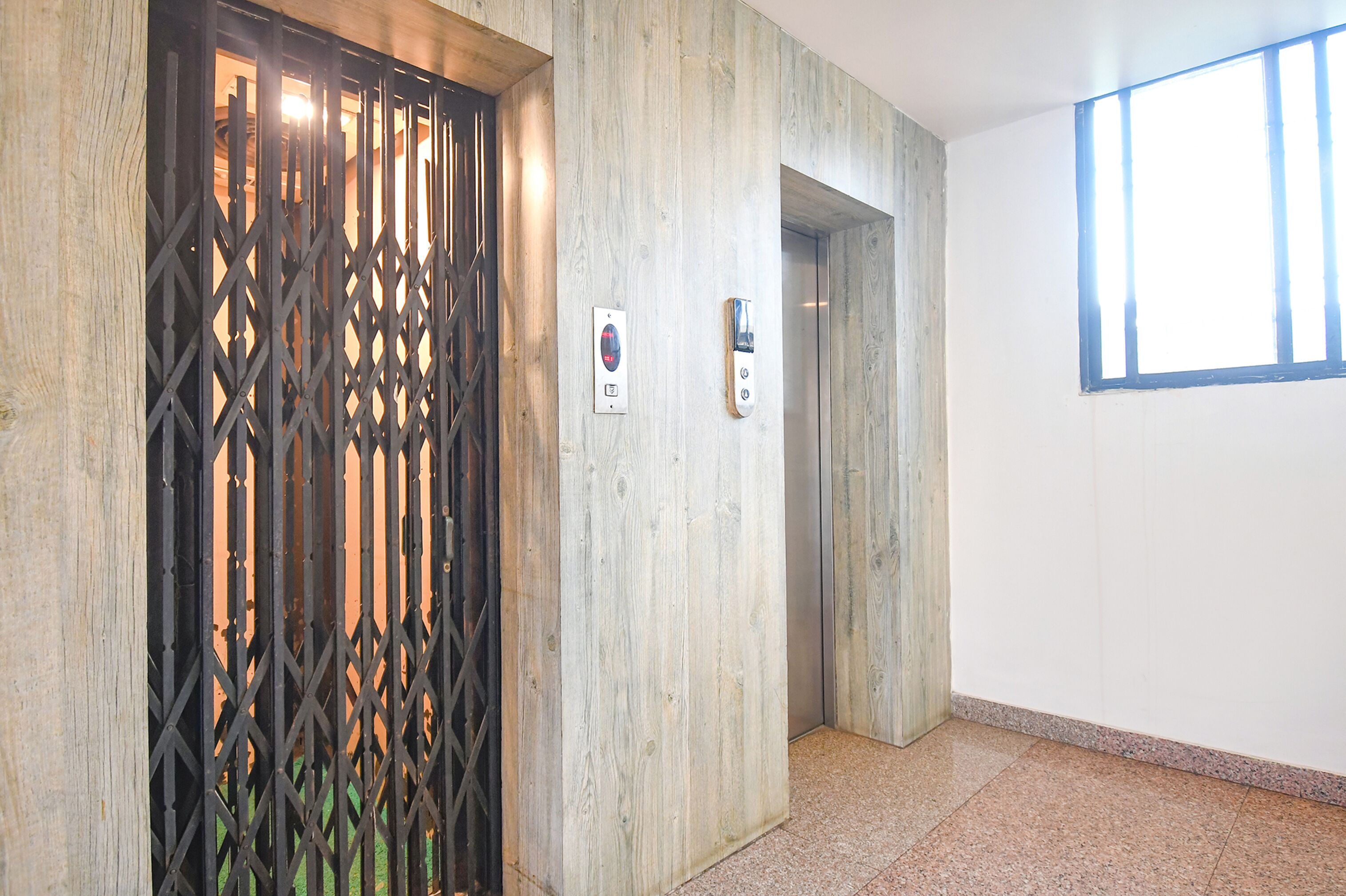 A hallway with a wooden door, an elevator, and a window.