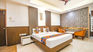 A hotel room with a bed, bedside table, chair, and a decorative wall. - Fabhotel Emerald (Ranchi)