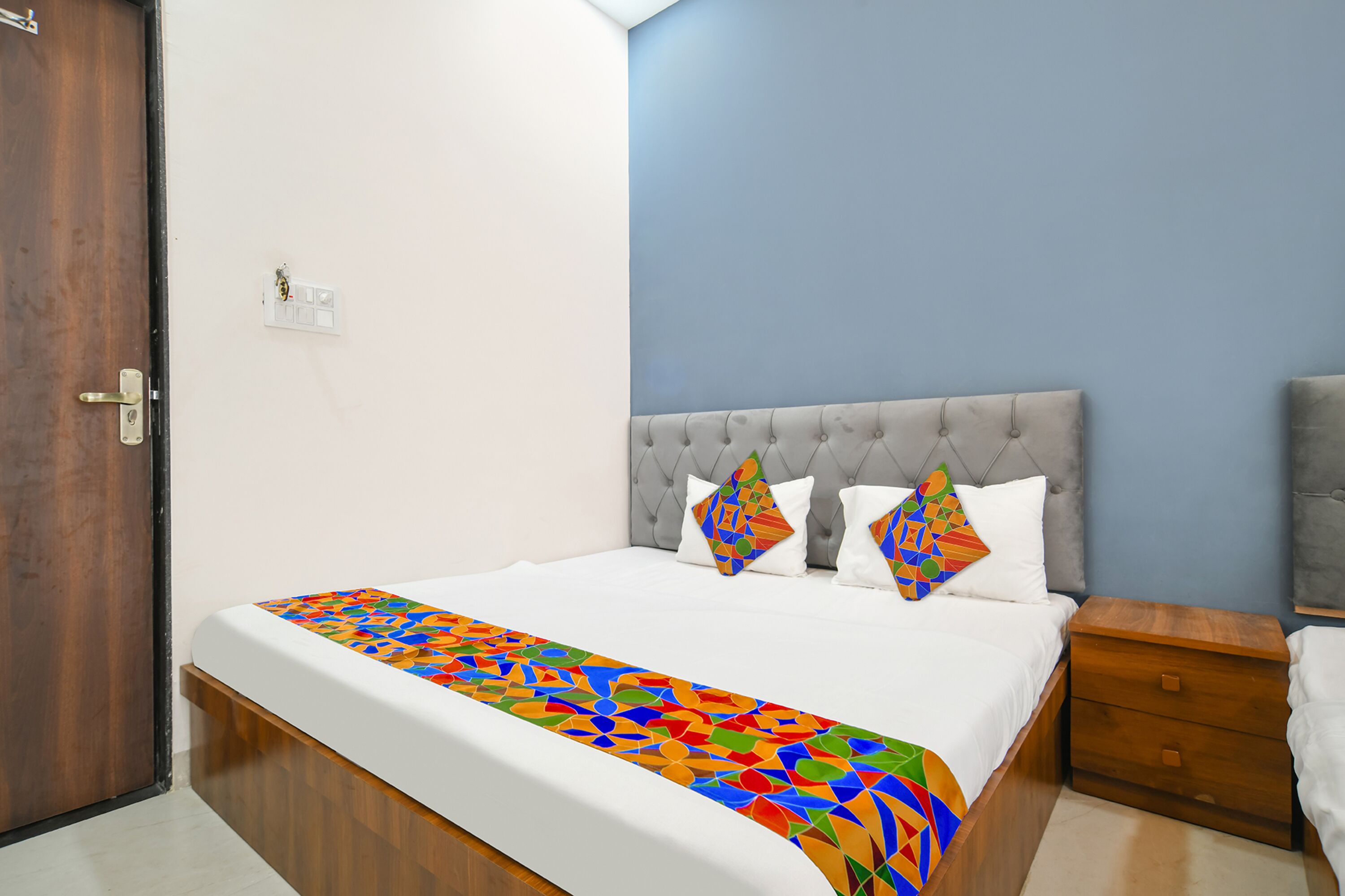 Une chambre à coucher avec un lit, une table de chevet, une porte en bois et un interrupteur mural.