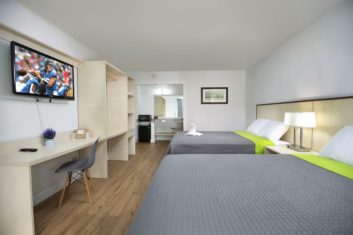 A hotel room with a desk, two beds, a TV, a mirror, and a framed picture on the wall.