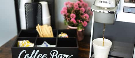 Una barra de café con una máquina de café Keurig, una taza de café y una caja con el rótulo 'Coffee Bar' sobre una superficie de madera.