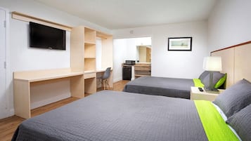 Hotellihuone, jossa on kaksi sänkyä, työpöytä, televisio, peili ja pieni keittokomero.