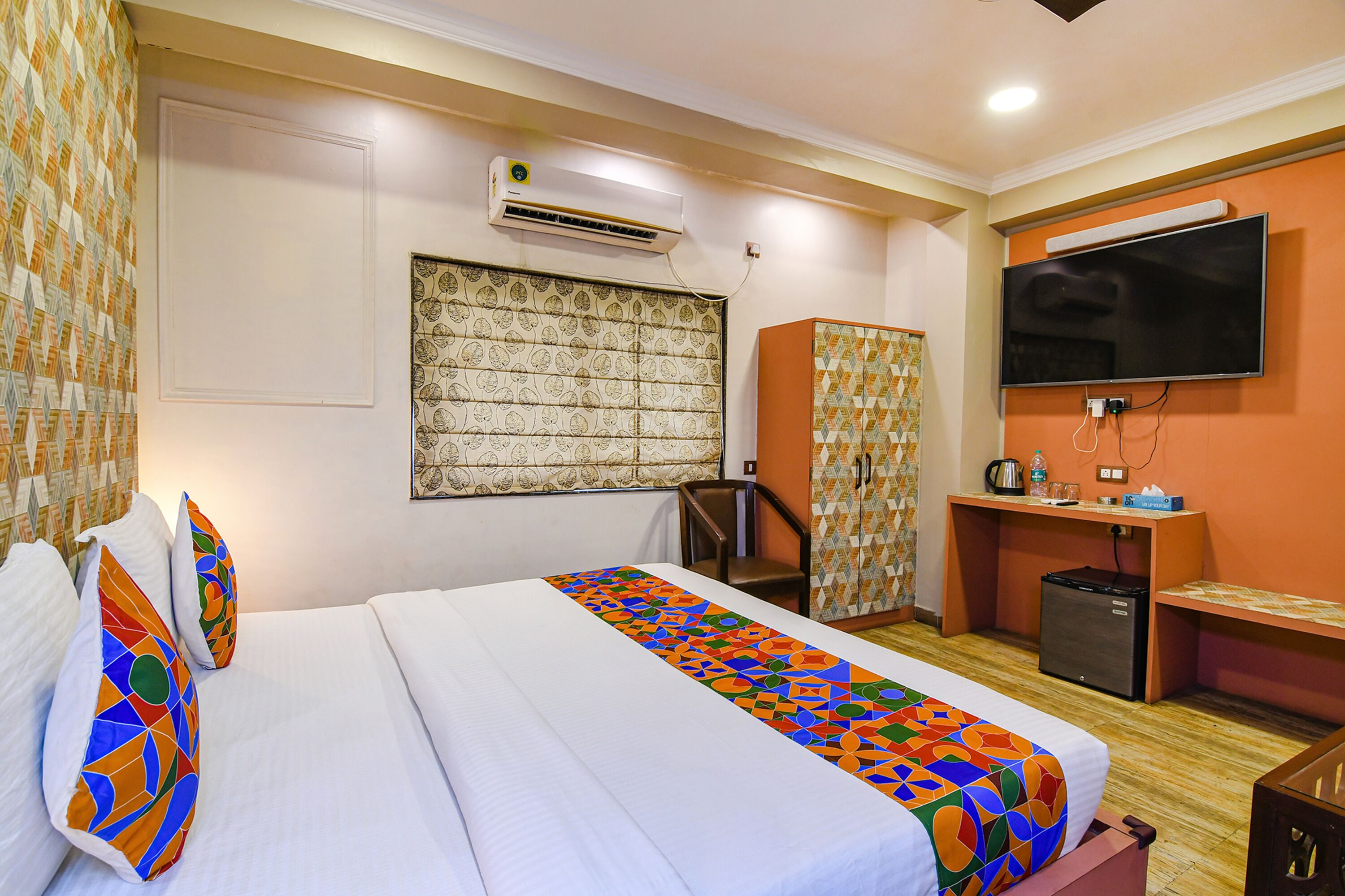 A hotel room with a bed, a desk, a television, and an air conditioning unit.