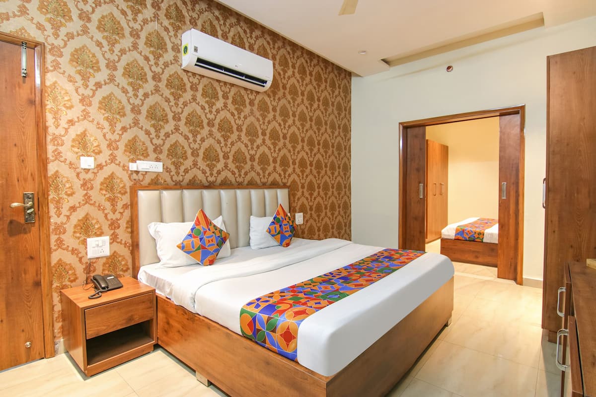 A hotel room with a large bed, a wooden nightstand, a telephone, and a mirror.