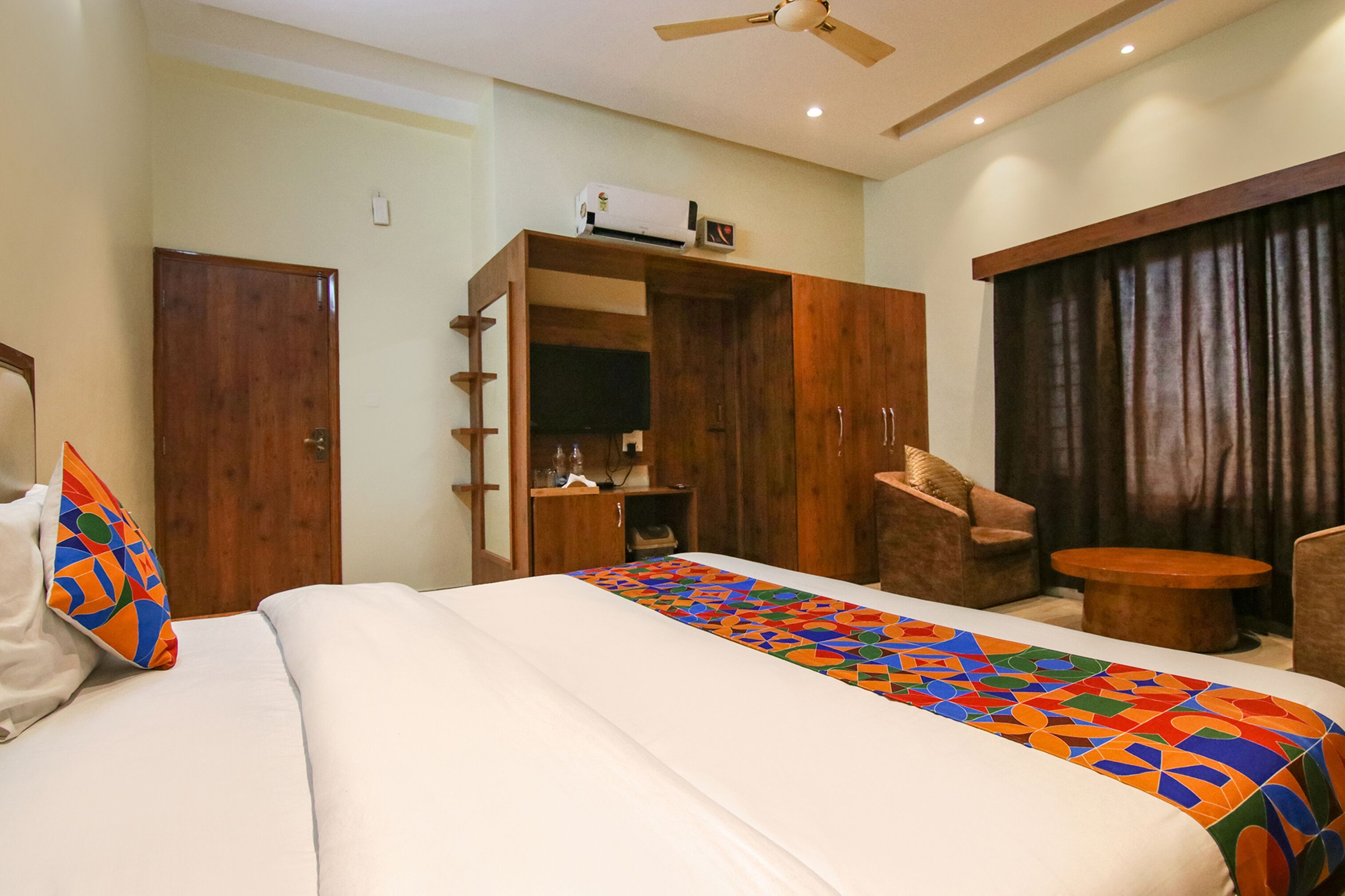 A hotel room with a large bed, a wardrobe, a desk, a chair, and a ceiling fan.
