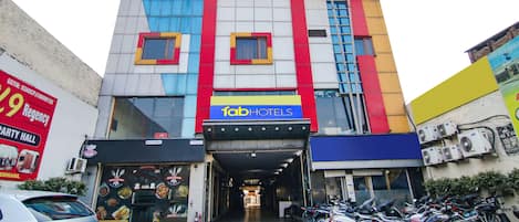 A multi-story building with a colorful facade, a sign for 'fab hotels', and a parking area with motorcycles.