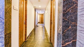 A hallway with marble walls, wooden doors, and a tiled floor. - Fabexpress Subh Residency (Howrah)