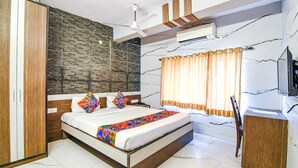 A modern bedroom with a large bed, a wooden wardrobe, a ceiling fan, and a TV mounted on the wall. - Fabexpress Subh Residency (Howrah)
