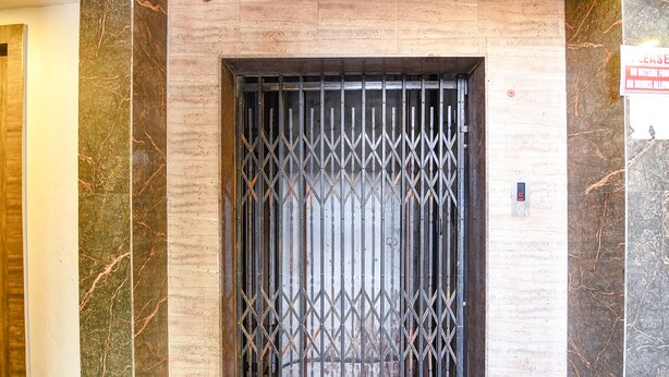 A metal gate with a diamond pattern, a marble wall, and a floor with a brownish tone. - Fabexpress Subh Residency (Howrah)