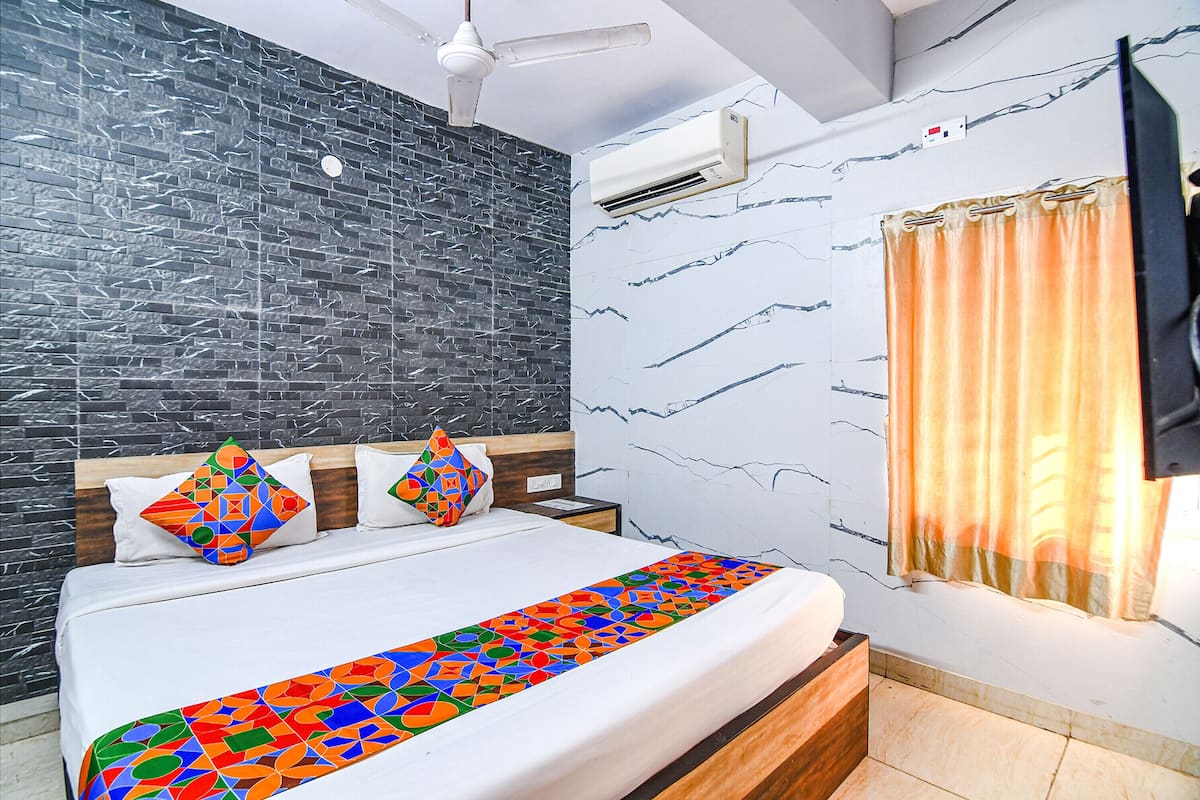 A hotel room with a bed, a nightstand, a wall-mounted air conditioner, and a window with curtains.